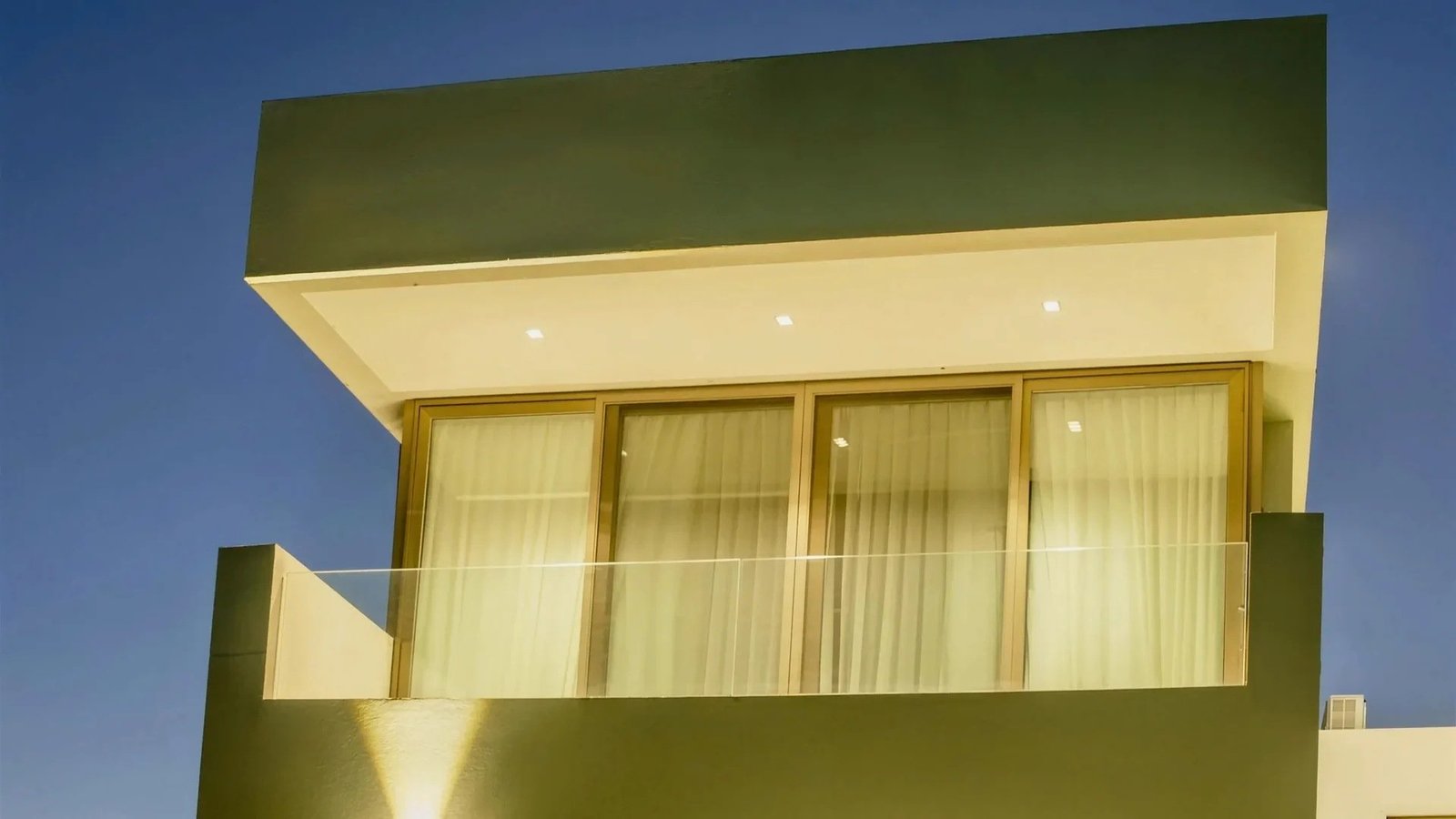Residencia en Gonnet. Paño corredizo con baranda de vidrio en el frente del primer piso, a la hora azul.